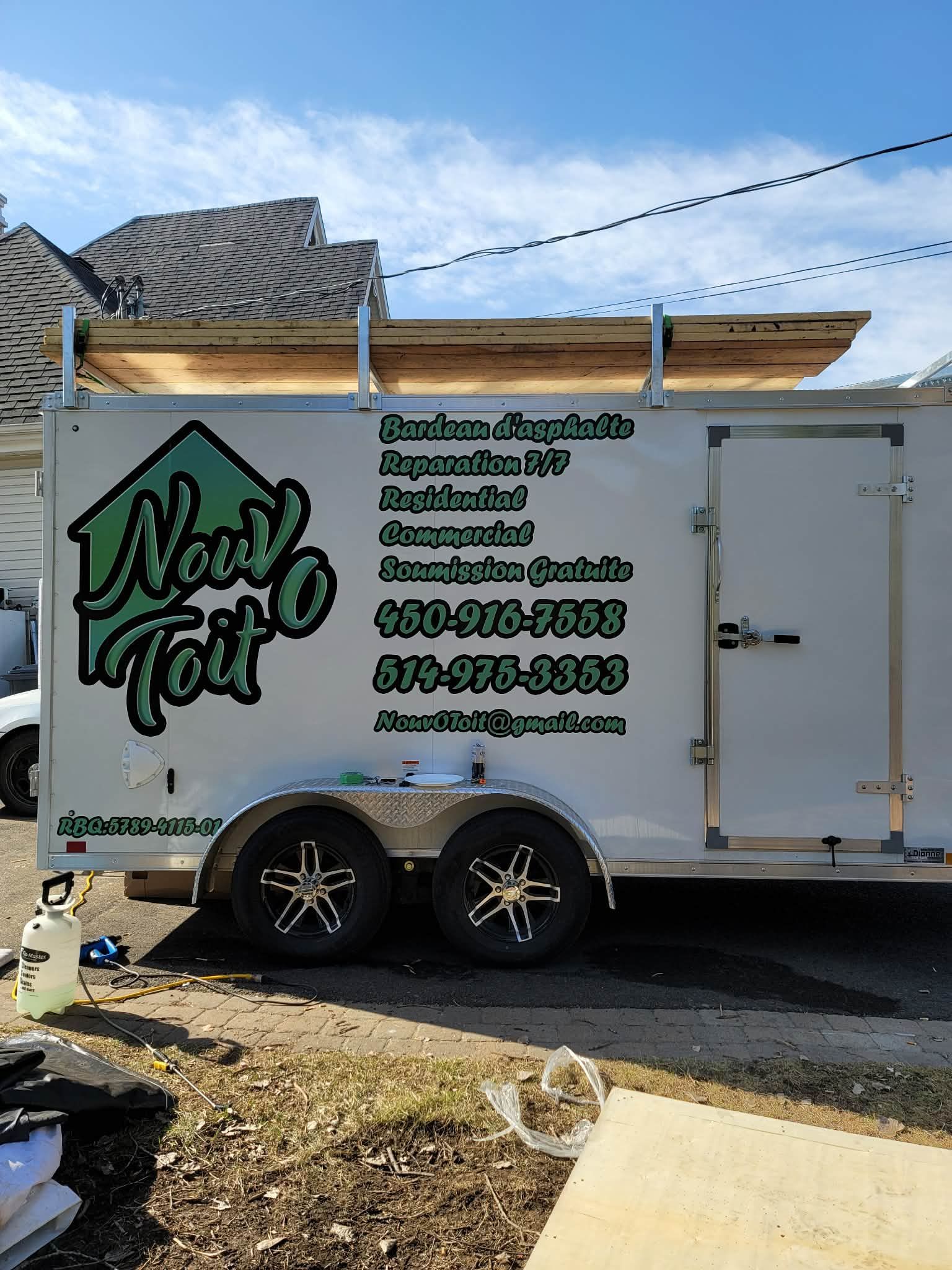 Une remorque blanche portant l'inscription « Novo Toit » avec des informations sur les services de toiture et des numéros de téléphone, était garée à l'extérieur.