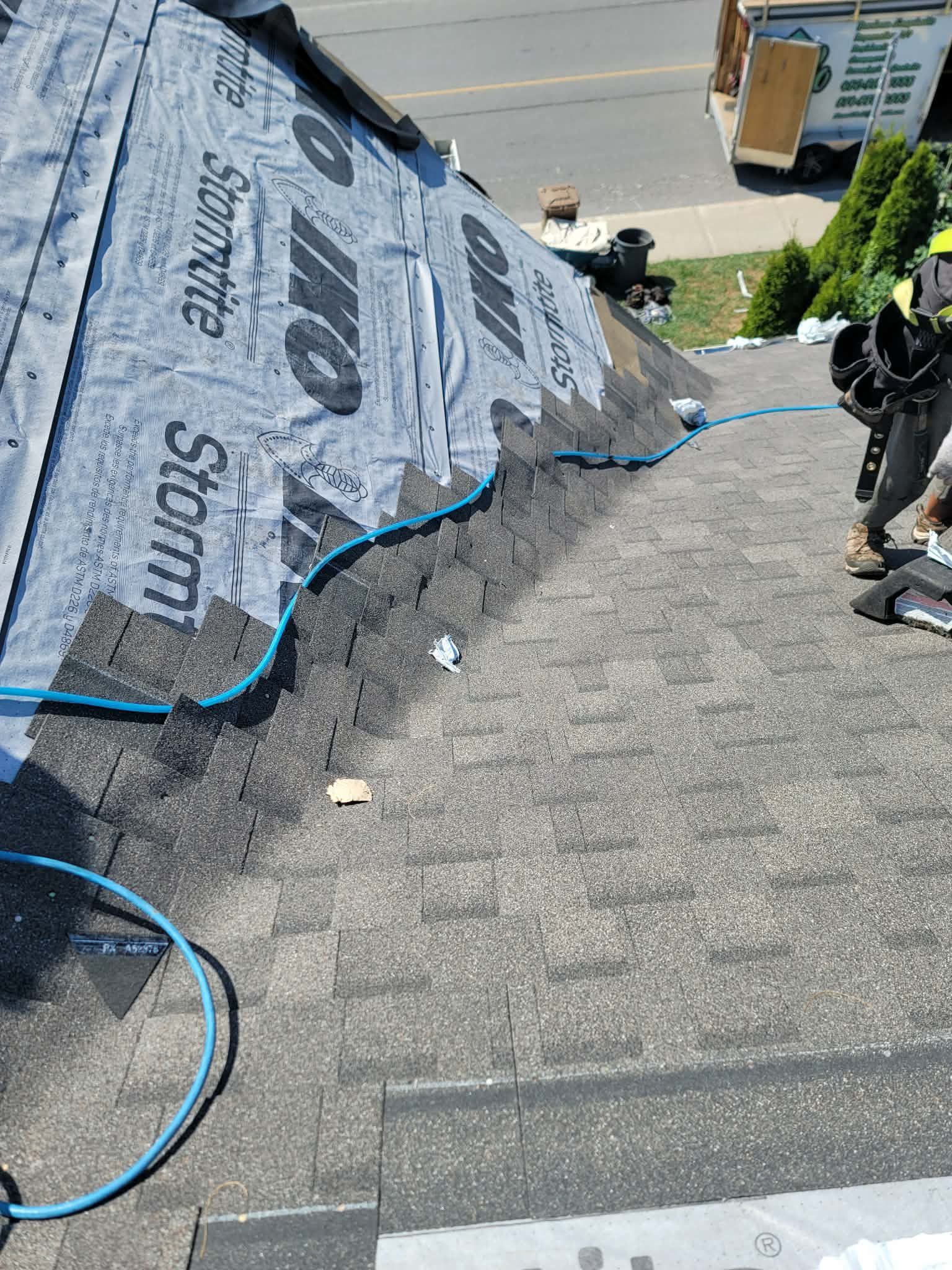 Un couvreur travaille sur un toit résidentiel, installant des bardeaux gris sur une sous-couche grise IKO Stormtite.