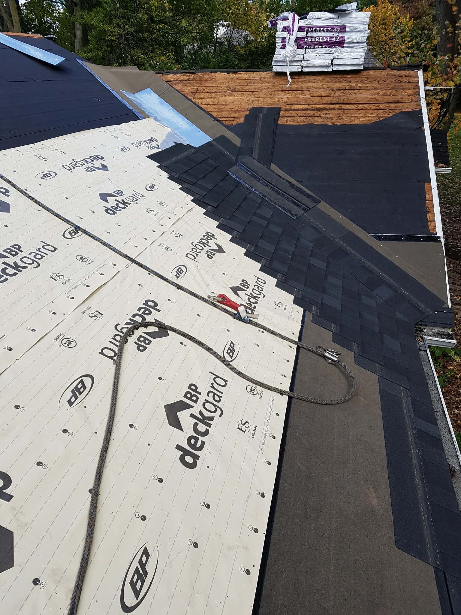 Une toiture en construction avec une sous-couche blanche et des bardeaux noirs partiellement posés sur une charpente en bois.