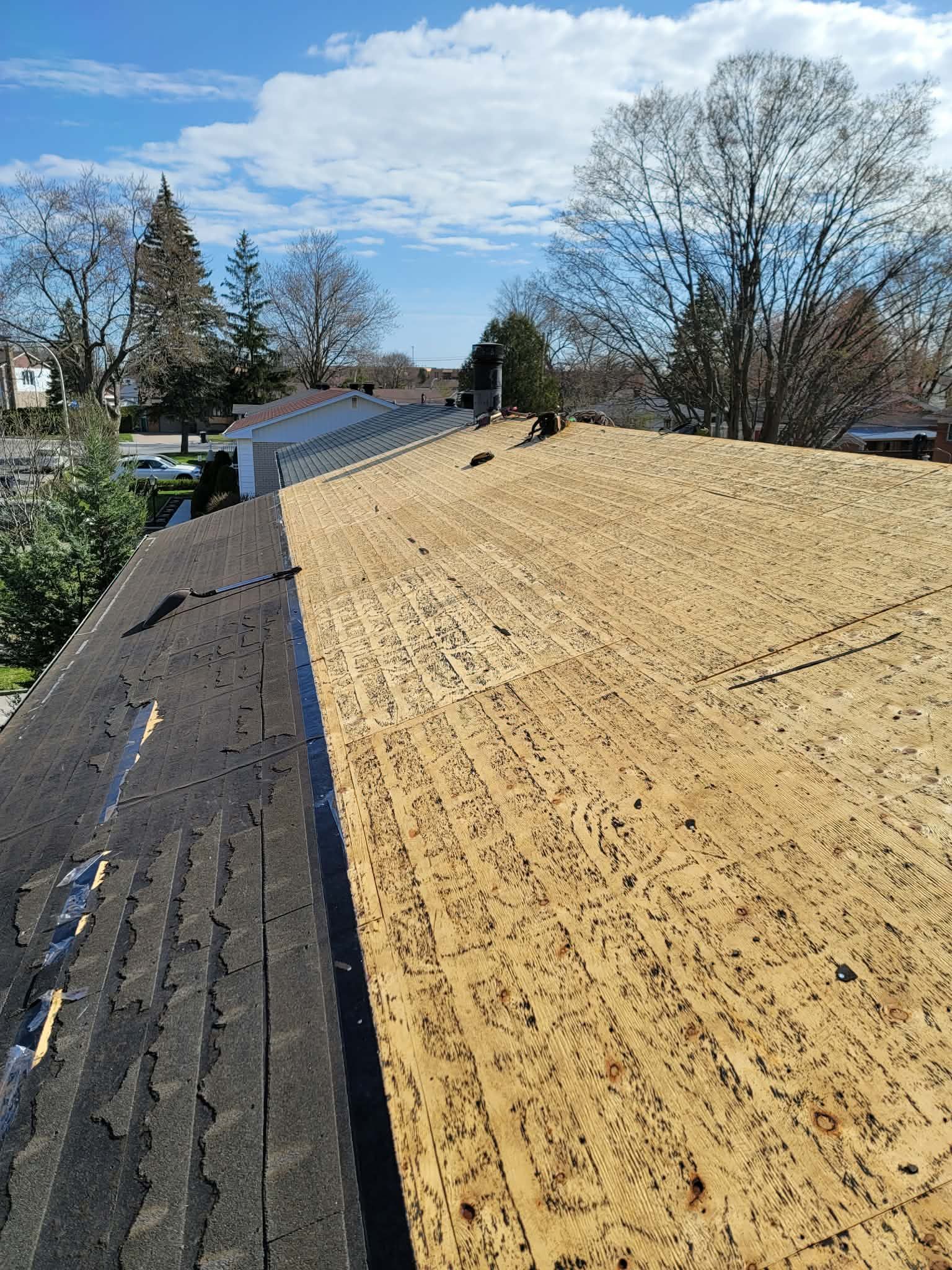 Un toit en construction laisse apparaître une section de contreplaqué apparent à côté d'une bande de vieux bardeaux restants.
