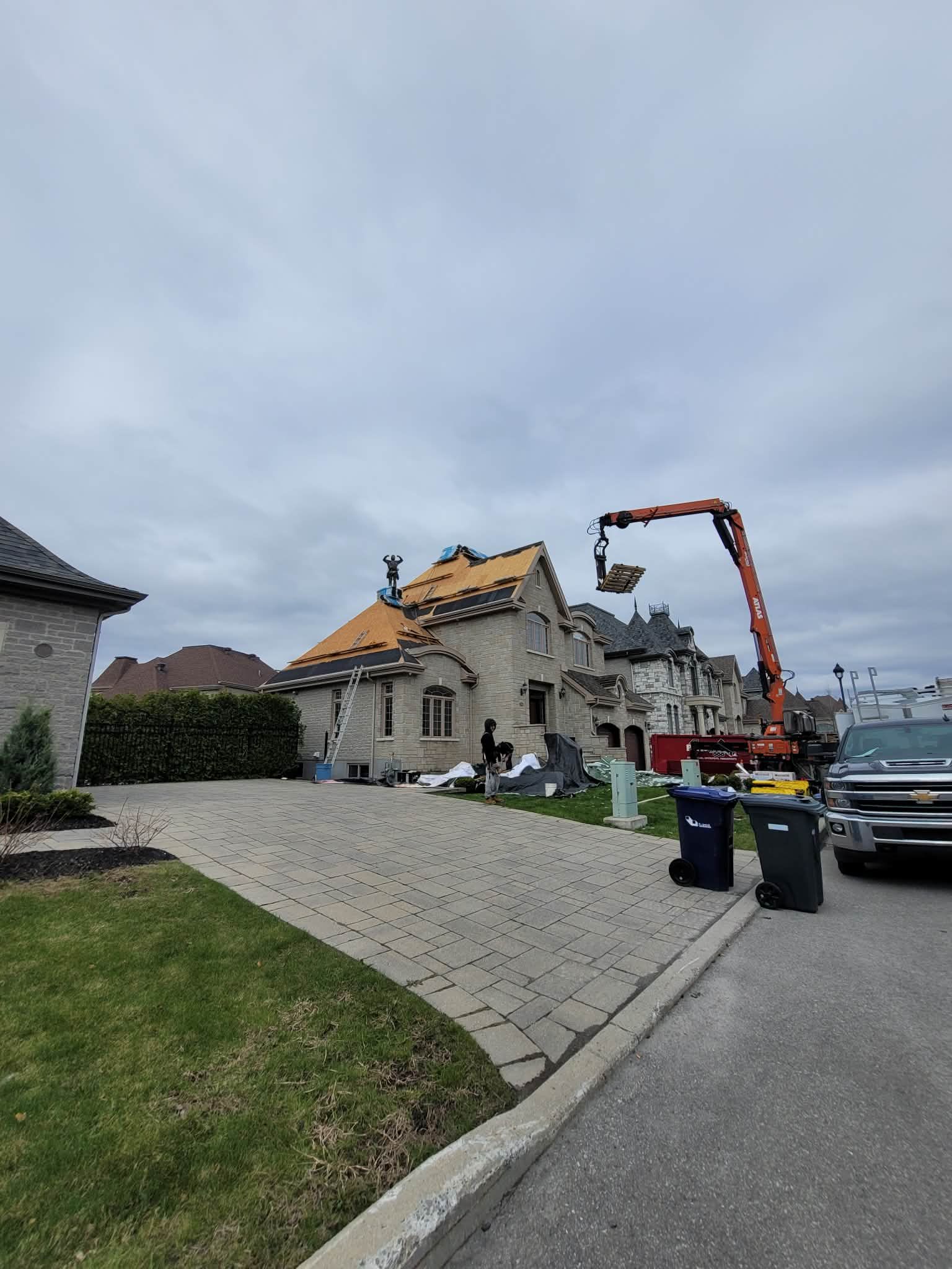 Une grue transporte des matériaux jusqu'aux ouvriers qui réparent le toit en bardeaux d'une maison en pierre de banlieue.