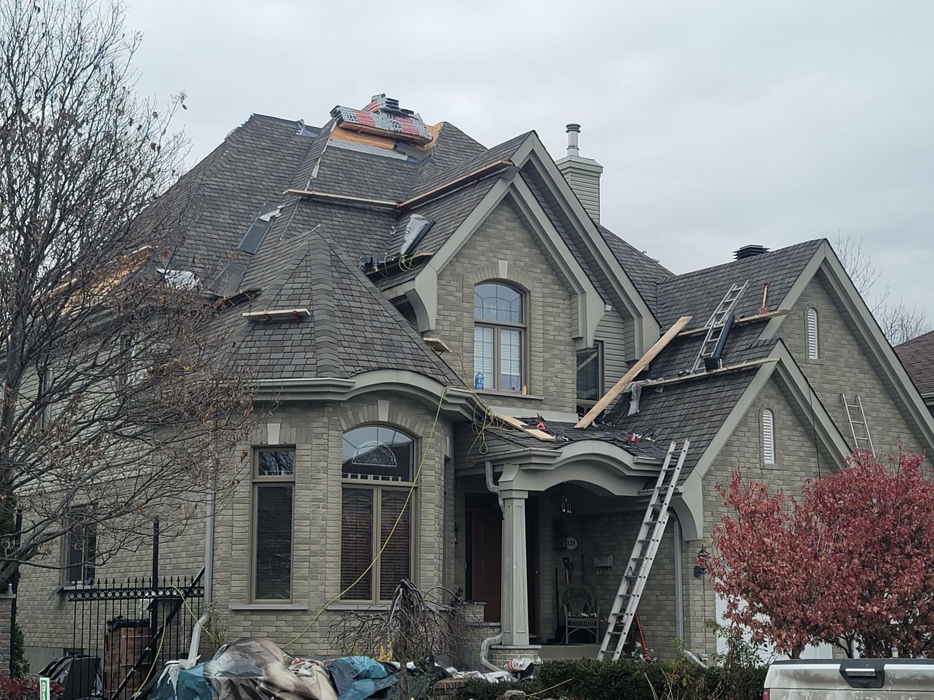 Une maison en pierre de deux étages avec un toit en construction, laissant apparaître la sous-couche et une échelle appuyée contre celui-ci.