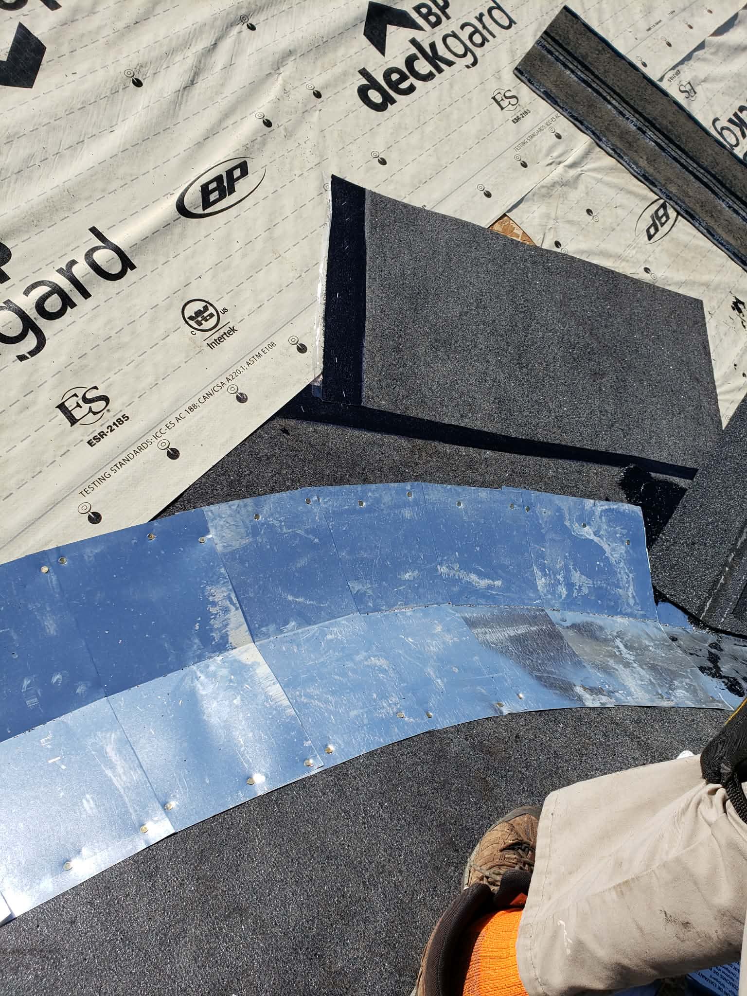 Un ouvrier installe des solins métalliques sur la sous-couche et les bardeaux de toiture sur un chantier de construction.