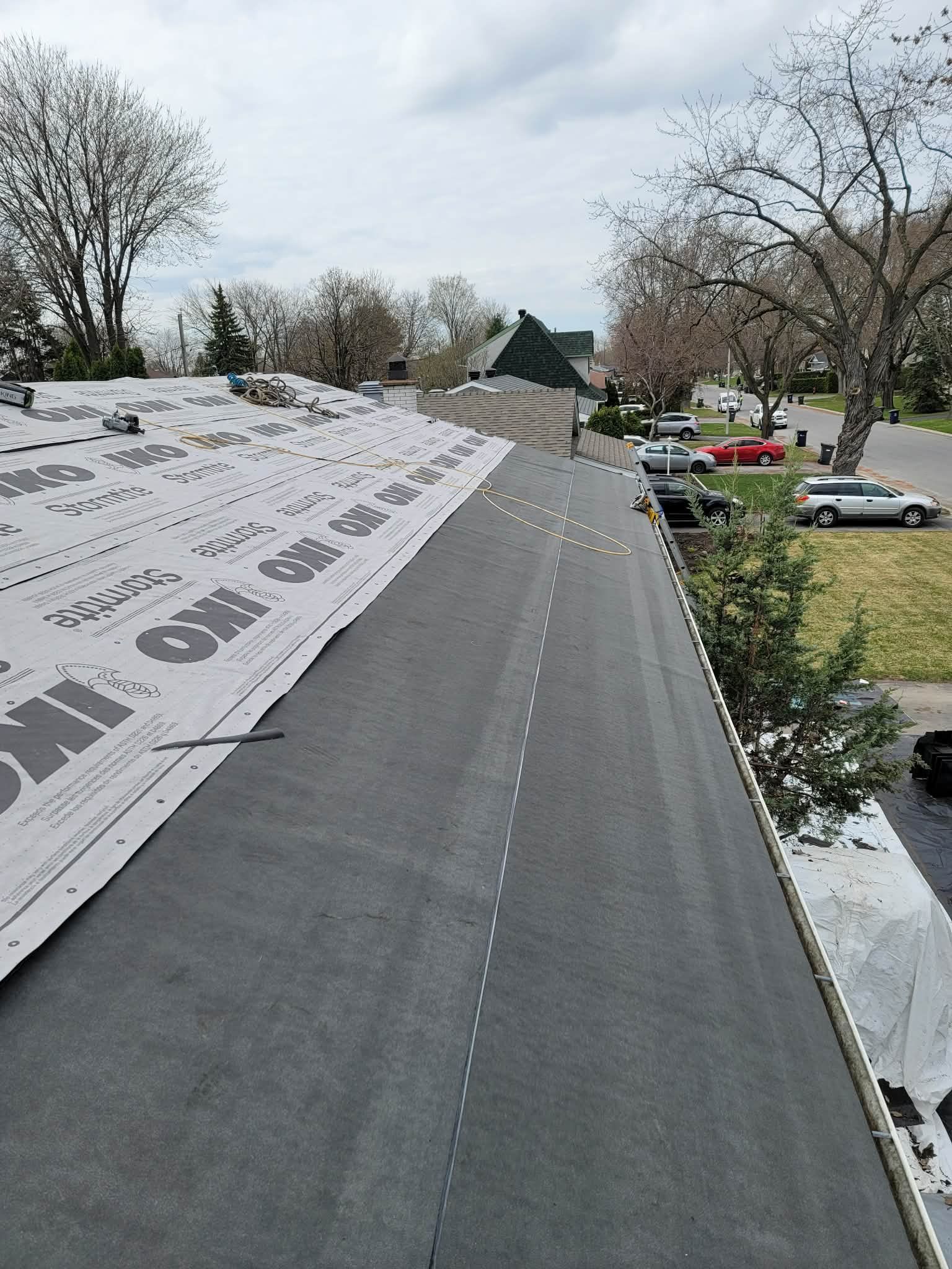 Toiture résidentielle en cours de réparation, avec une nouvelle sous-couche grise à gauche et une surface lisse et sombre à droite.