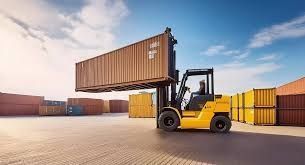 Yellow forklift lifting a brown shipping container in a container yard under a blue sky