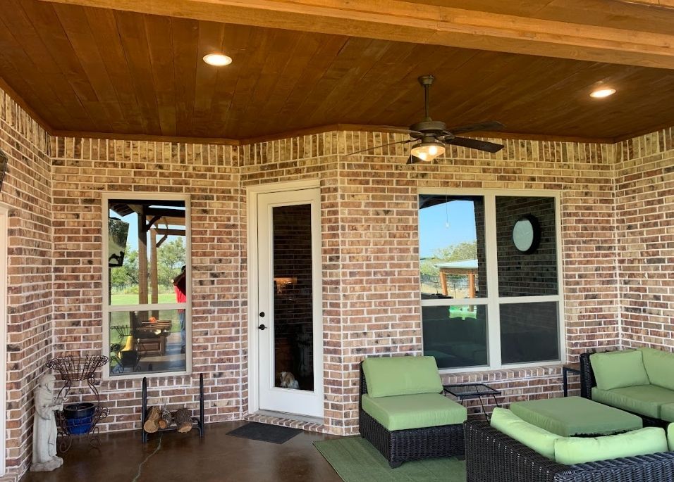 Brick patio with green seating, door, and windows. Brown wooden ceiling.