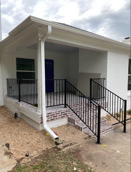 A brick-lined porch with black railings, white brick exterior, and a blue door.