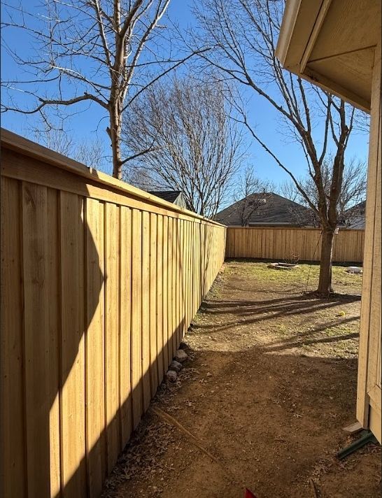 Wooden fence lines a backyard, sunny day with leafless trees.