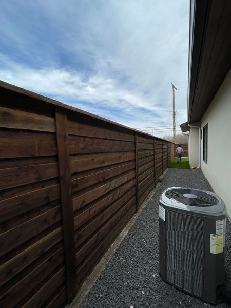 Dark wooden fence along a house, with an air conditioning unit in front.