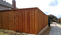 Wooden fence with a brown stain bordering a grassy area and alley.