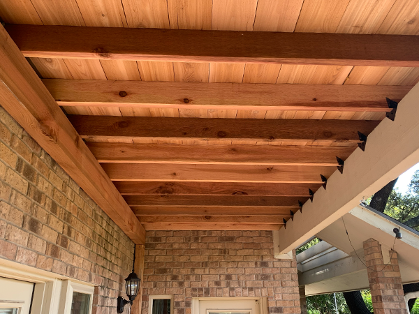 Cedar wood ceiling on a porch, supported by beams and brick wall.