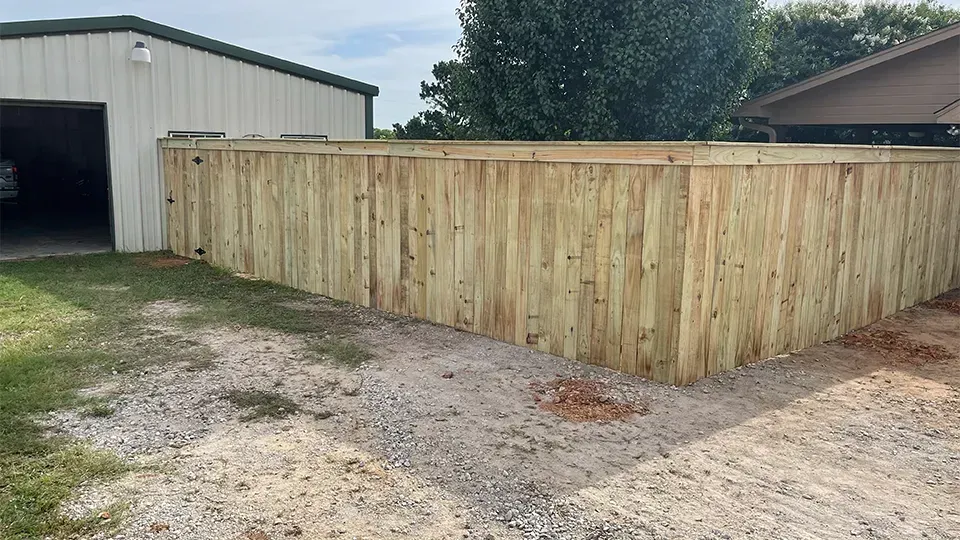Wooden fence surrounding a gravel area, beside a light-colored garage.