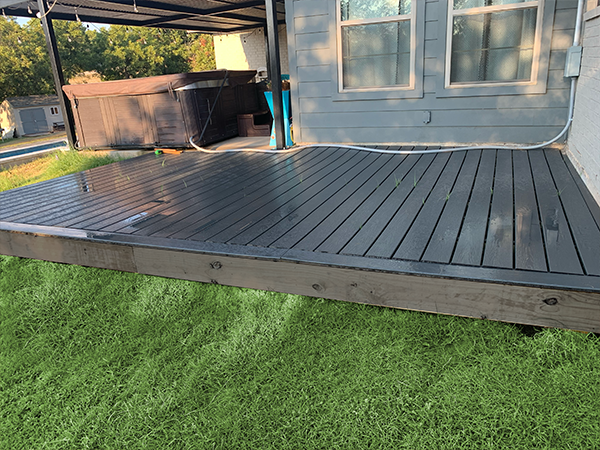 Gray composite deck with a hot tub under a covered patio. Green grass surrounds it.