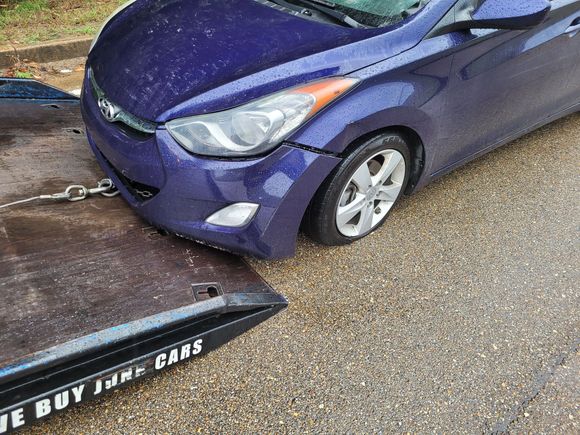 Blue car hooked to a tow truck by a chain on a wet road