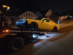 Yellow sports car on a tow truck at night in a residential neighborhood