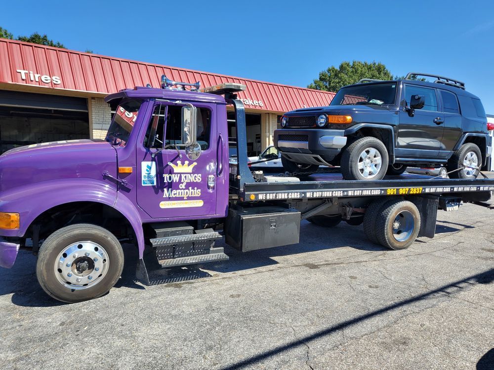 Purple tow truck carrying a black SUV outside a building with a red roof
