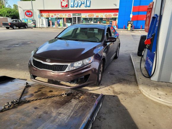 Brown sedan at a gas station, parked on a tow truck ramp near the pumps