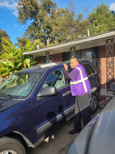 Person in purple vest leaning into a blue SUV in a driveway outside a house.