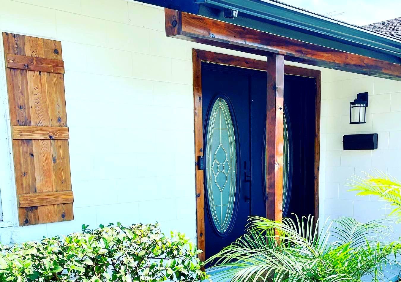A white house with a black door and a window with wooden shutters.