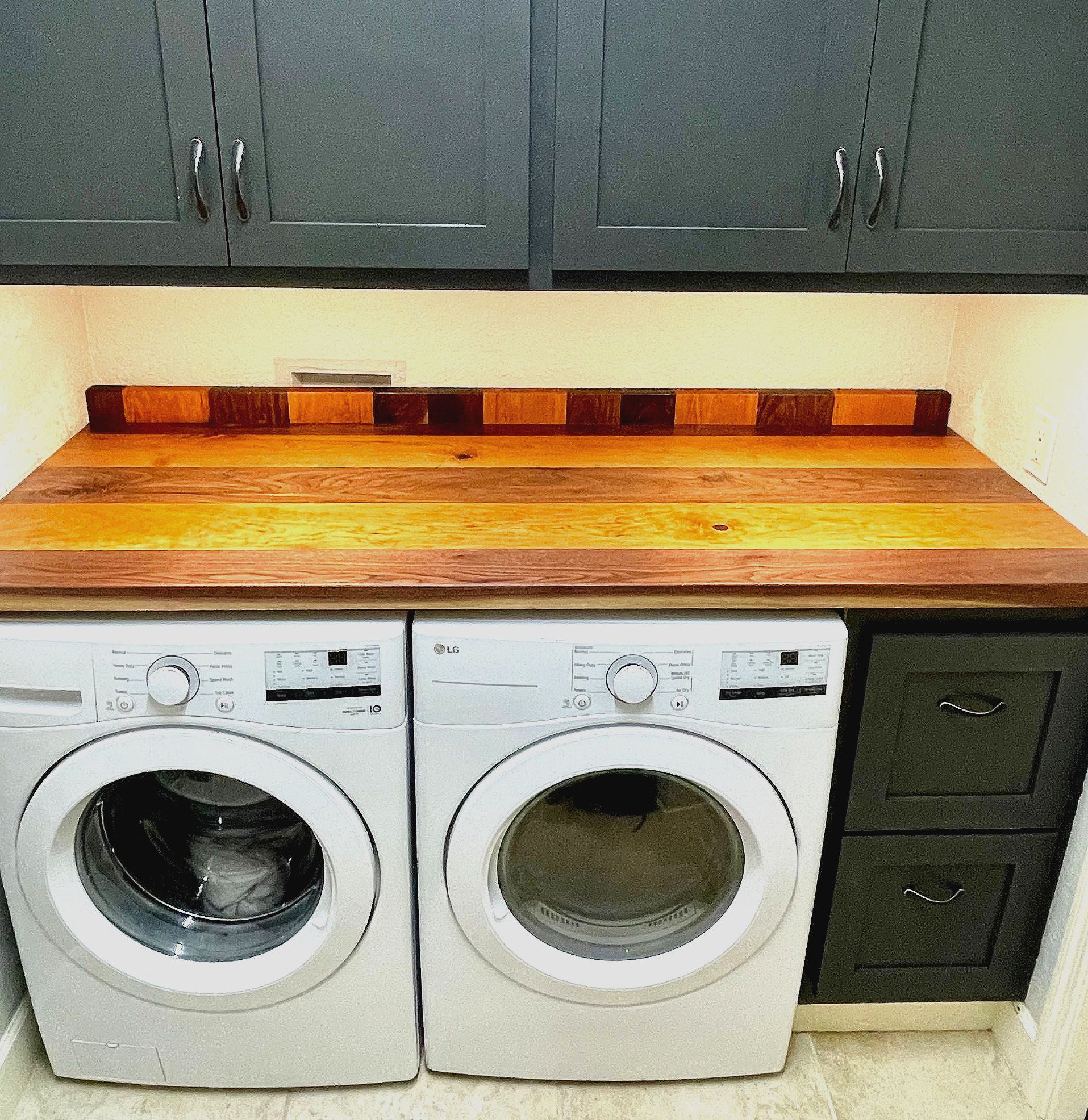 A laundry room with a wooden counter top and two washers and dryers