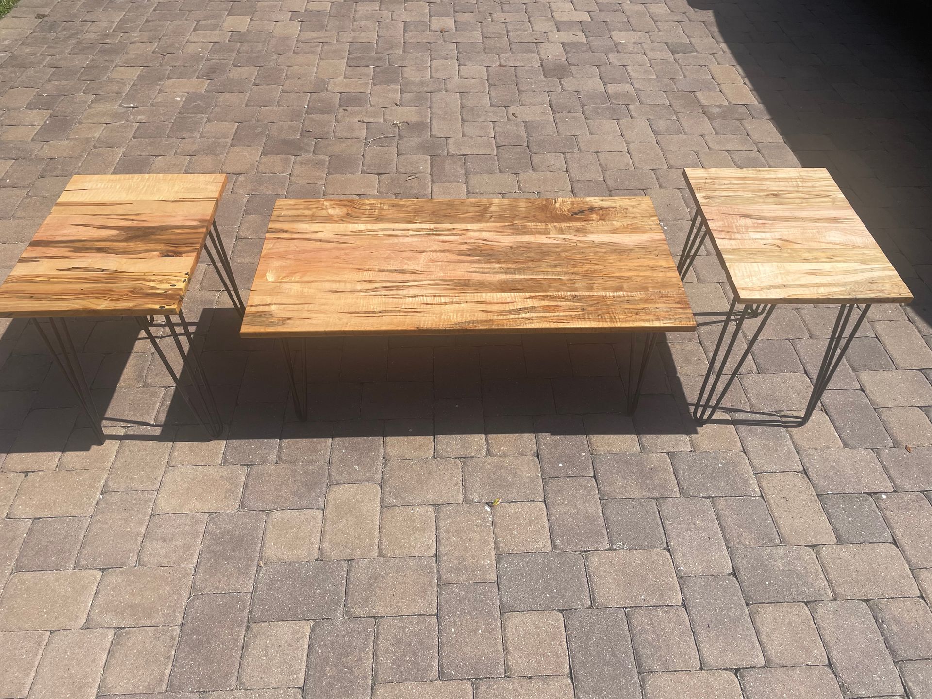 Three wooden tables are sitting on a brick driveway.
