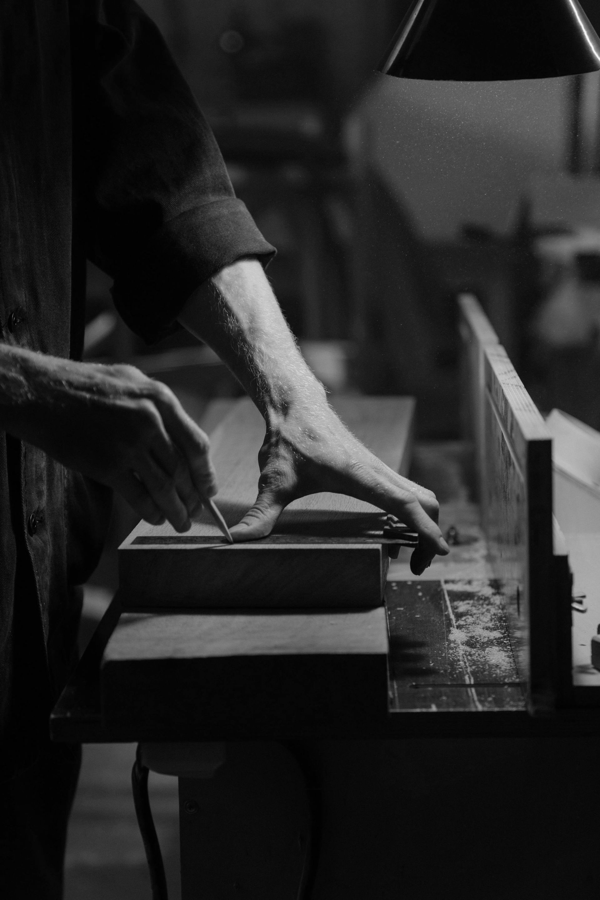A black and white photo of a person cutting a piece of wood.