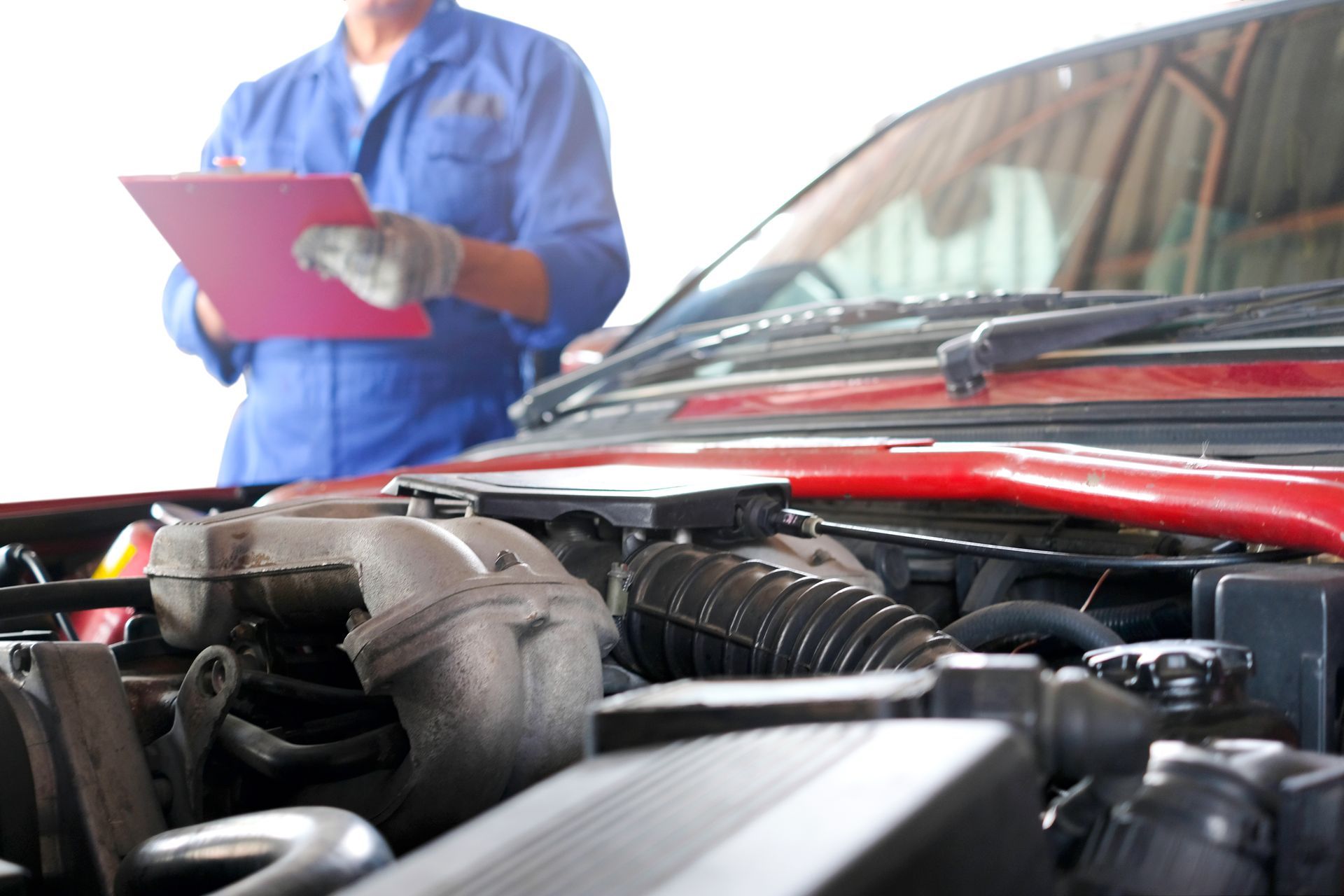 A mechanic is looking at a clipboard while standing next to a red car.