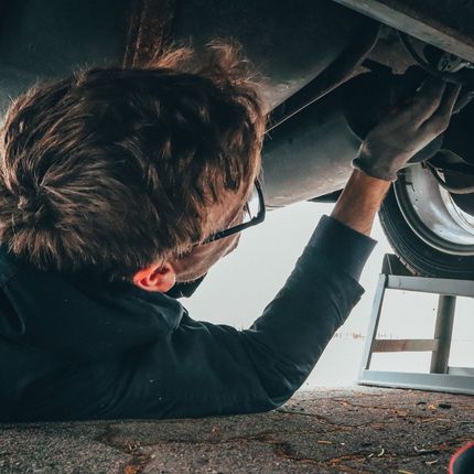 Mechanic working on the underside of a car, wearing glasses and gloves.