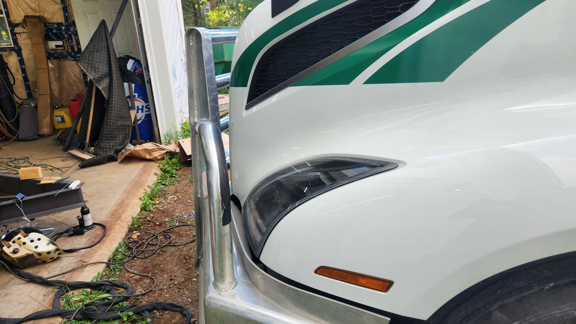 A white truck with green stripes is parked in front of a garage.