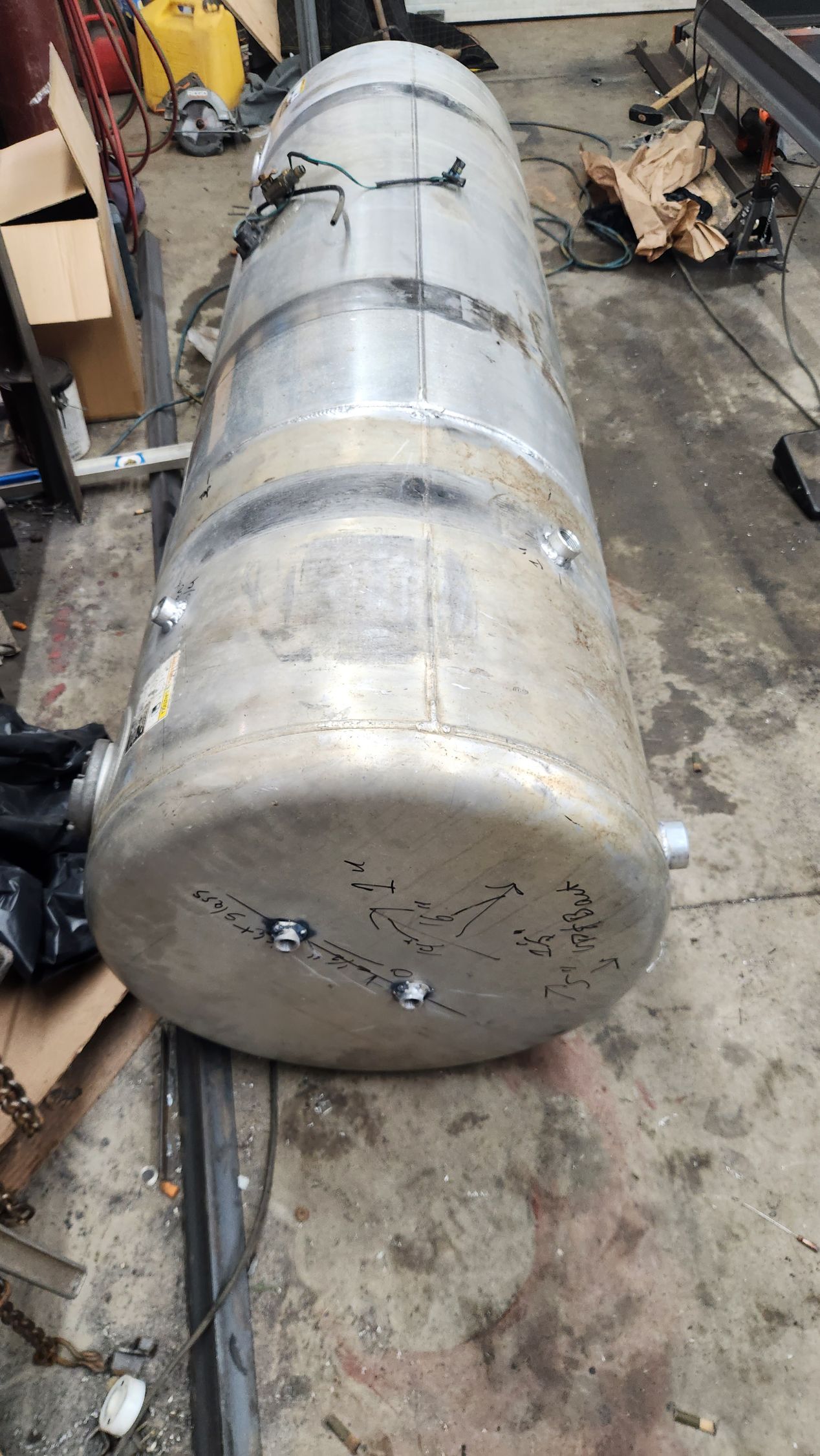 A large aluminum tank is sitting on the ground in a garage.