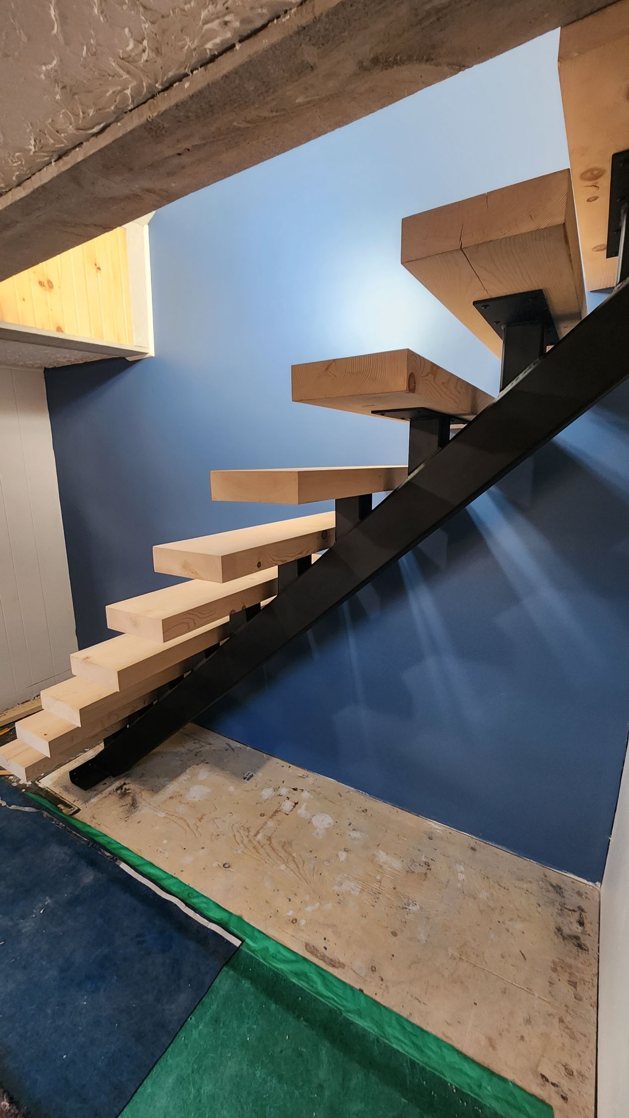 A wooden staircase is being built in a room with a blue wall.