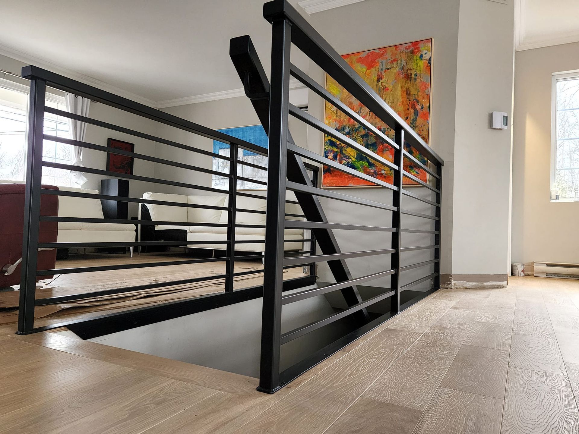 A staircase with a black railing in a living room with a painting on the wall.