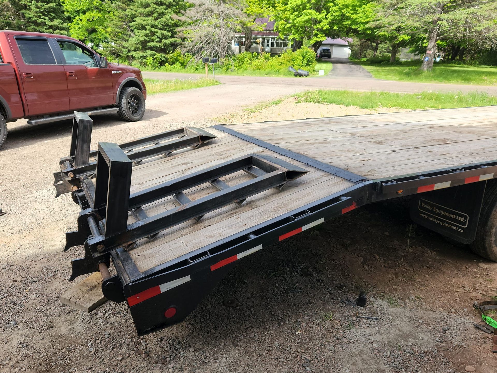 A red truck is parked next to a flatbed trailer.
