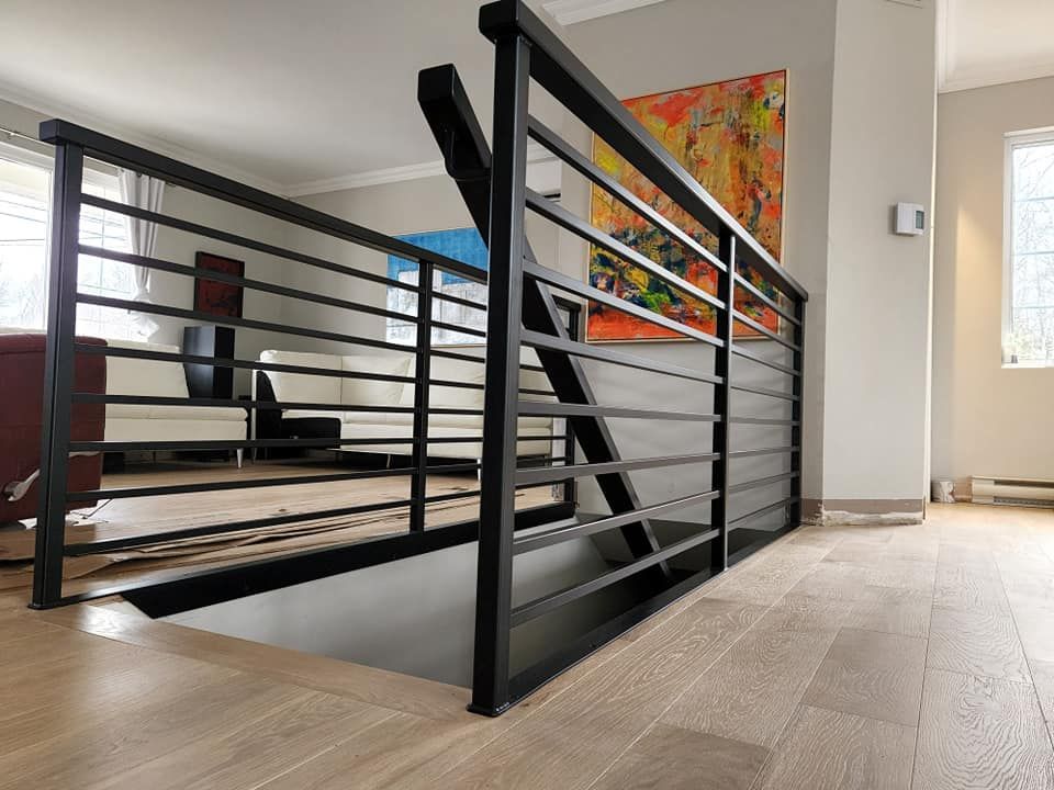 A staircase with a black railing in a living room with a painting on the wall.