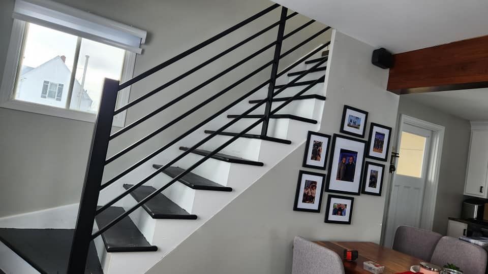 A staircase with a black railing in a living room with pictures on the wall.