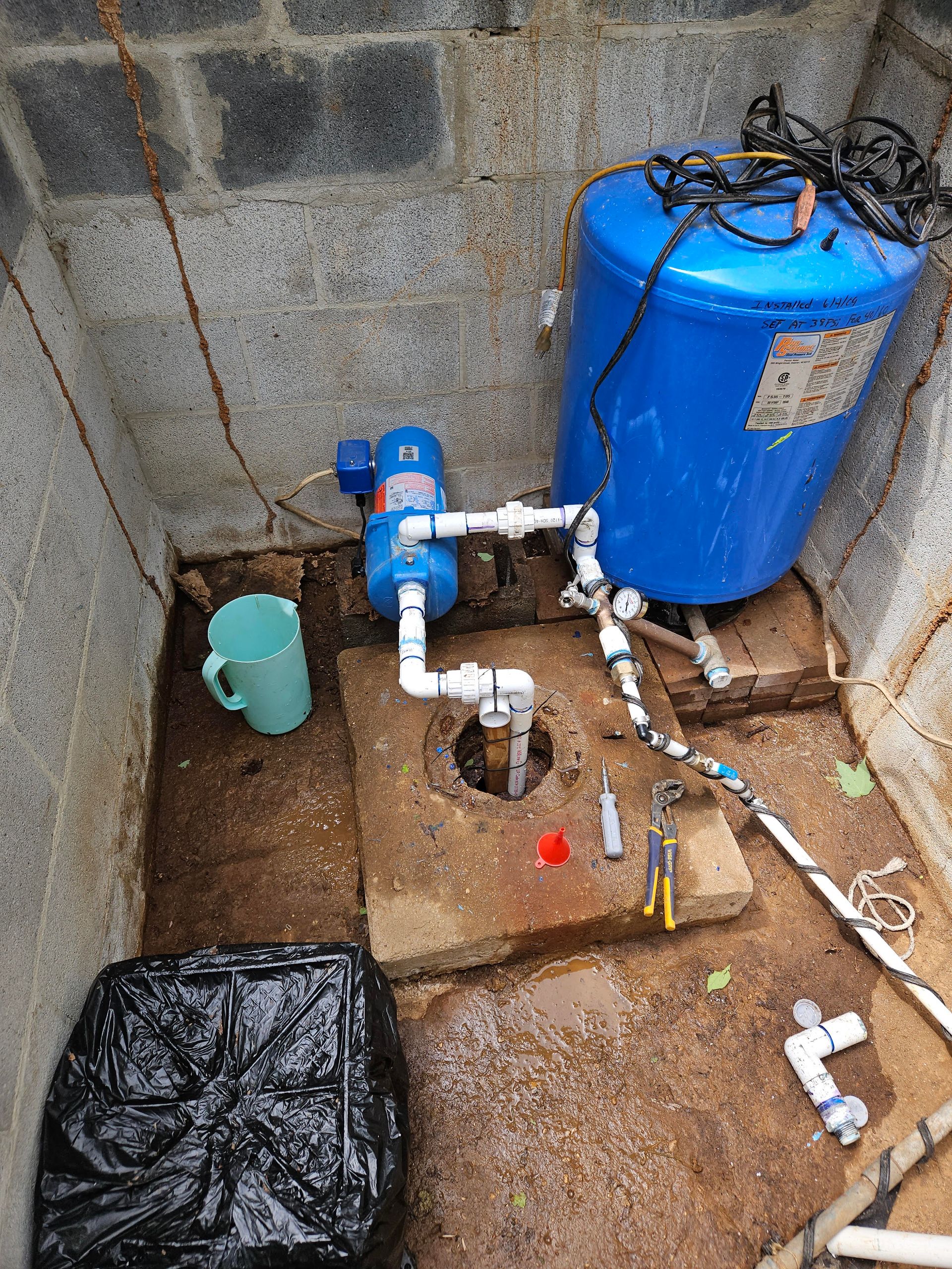 A blue water tank is sitting on the ground next to a brick wall.