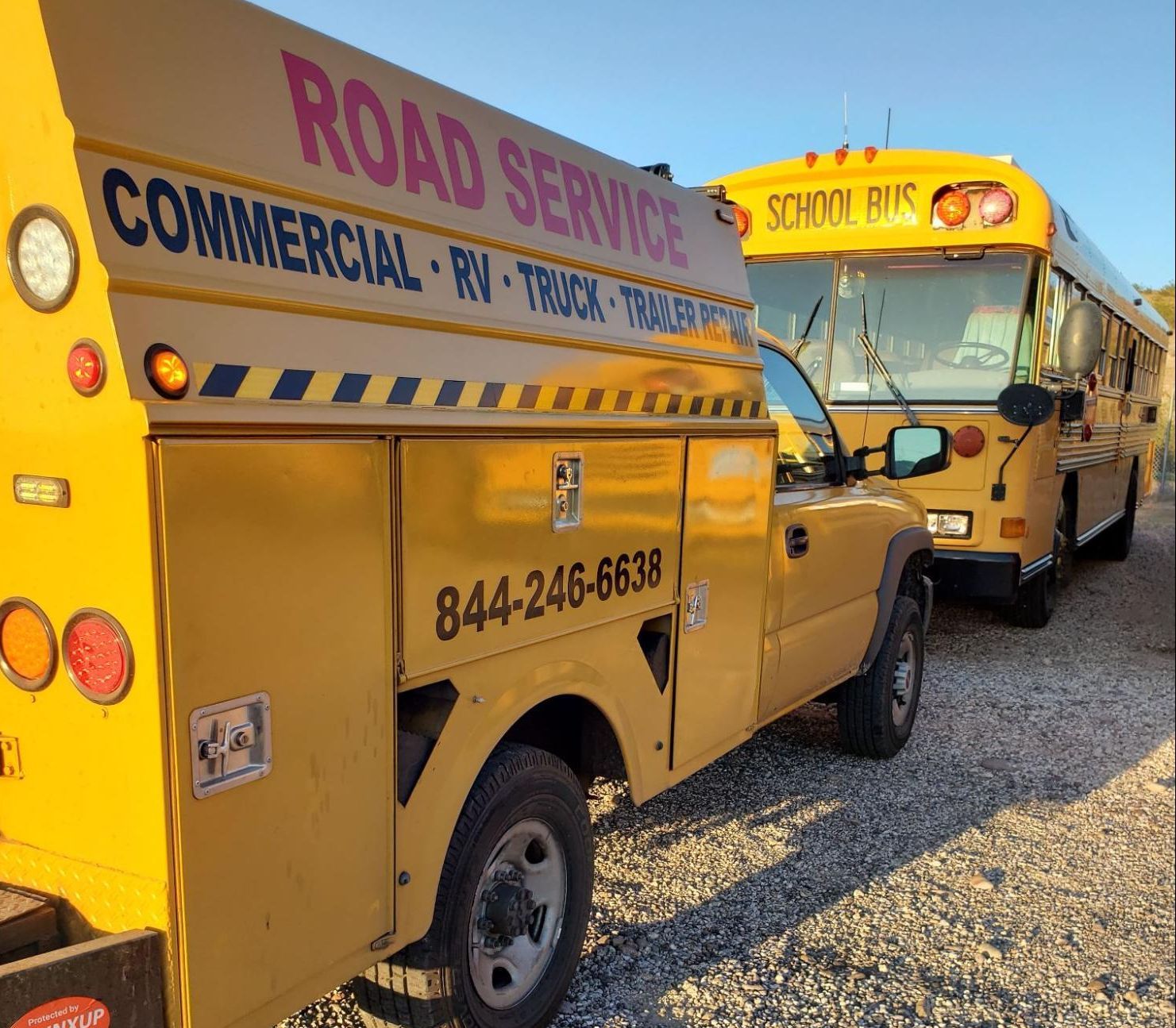 Two school buses are parked next to a road service truck