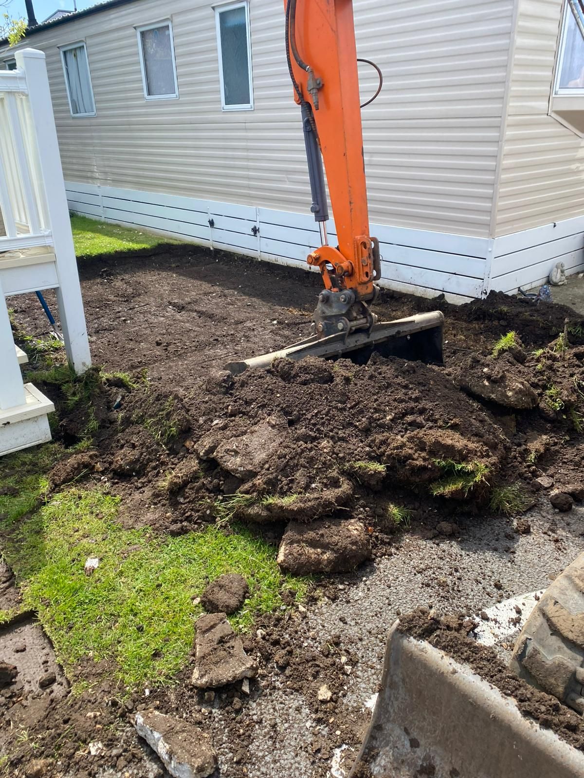 An excavator is digging a hole in the dirt in front of a mobile home.