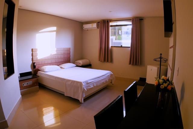 Quarto espaçoso com cama, janela, cortinas e escrivaninha, em ambiente com luz aconchegante.