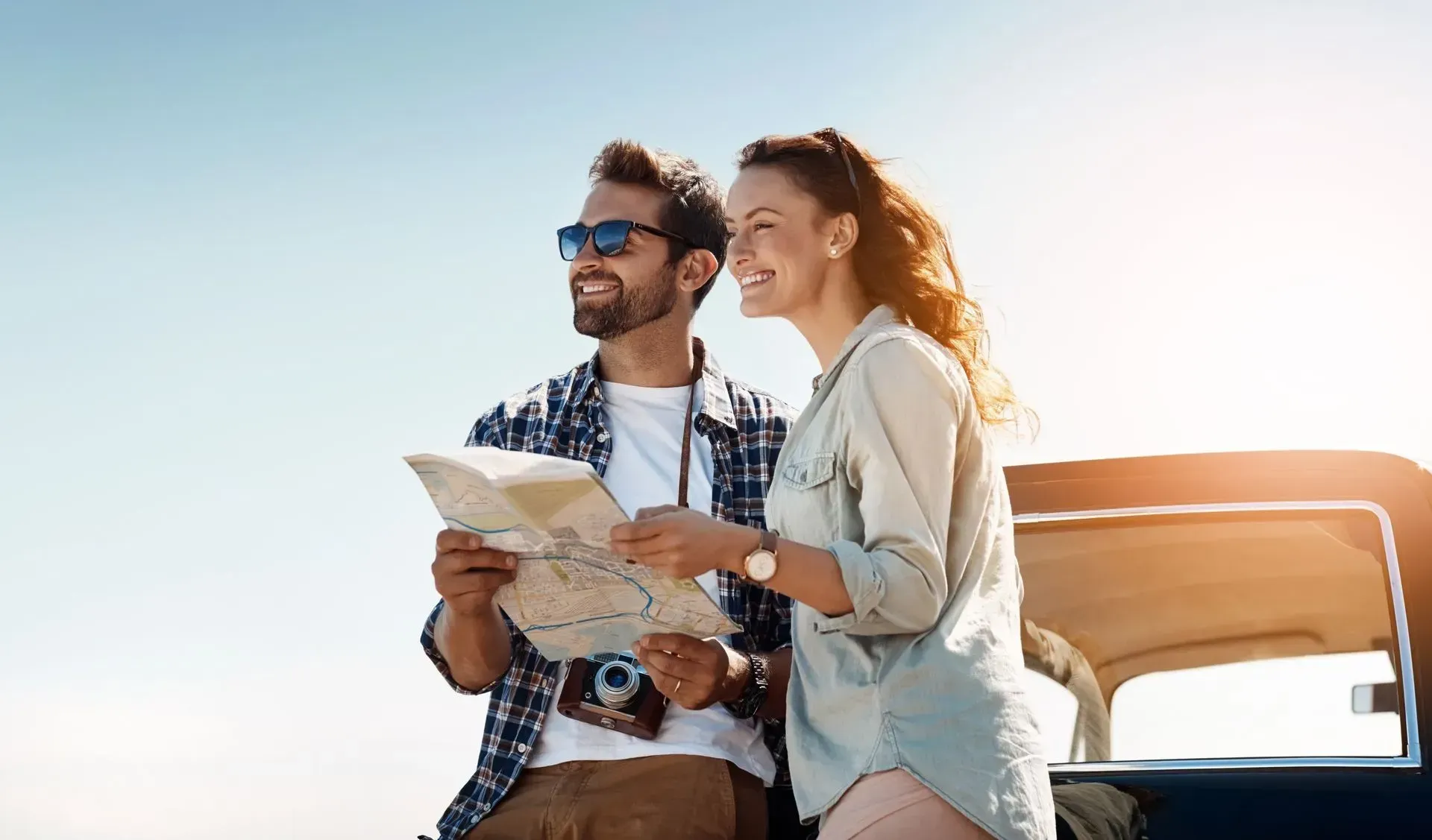 Casal lendo um mapa ao lado de um carro sob forte luz solar.