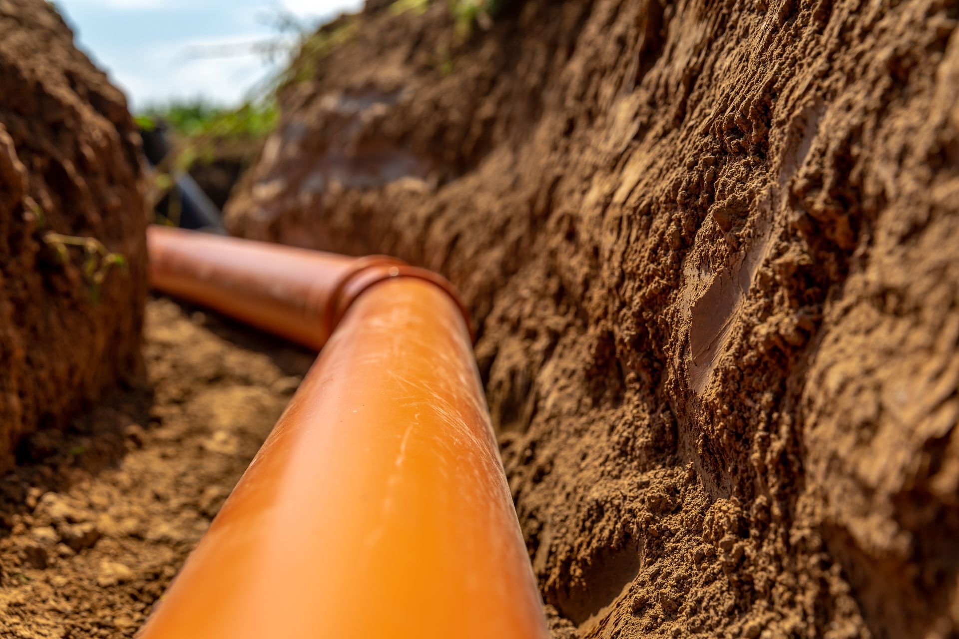 Orange pipe laid in a narrow, earthy trench, viewed from inside.