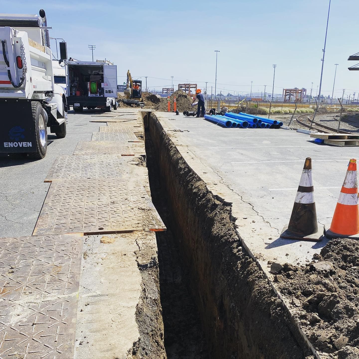 Construction site with trench, trucks, orange cones, and workers.