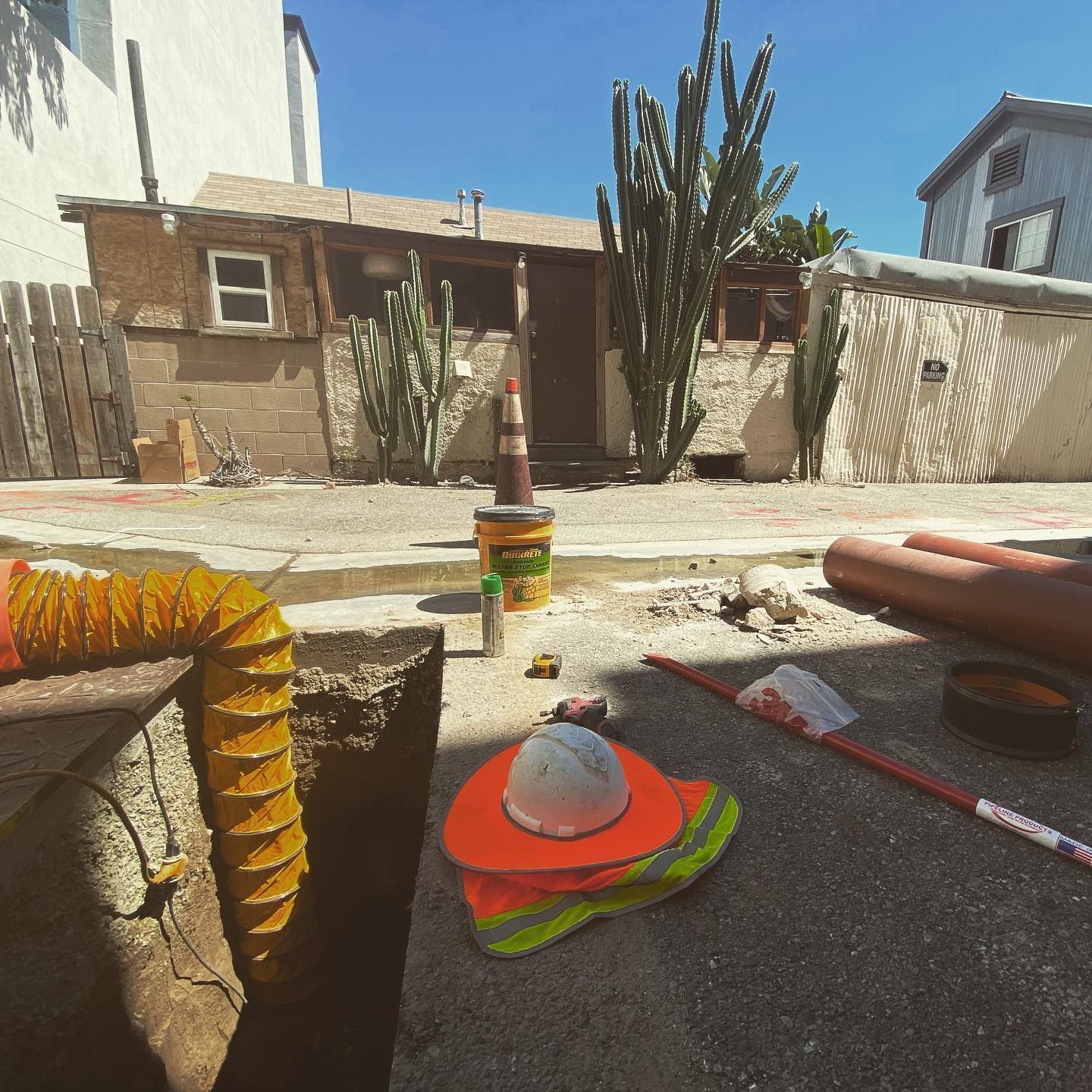 Construction site with tools, orange safety vest and hard hat, cactus plants, and a small building.