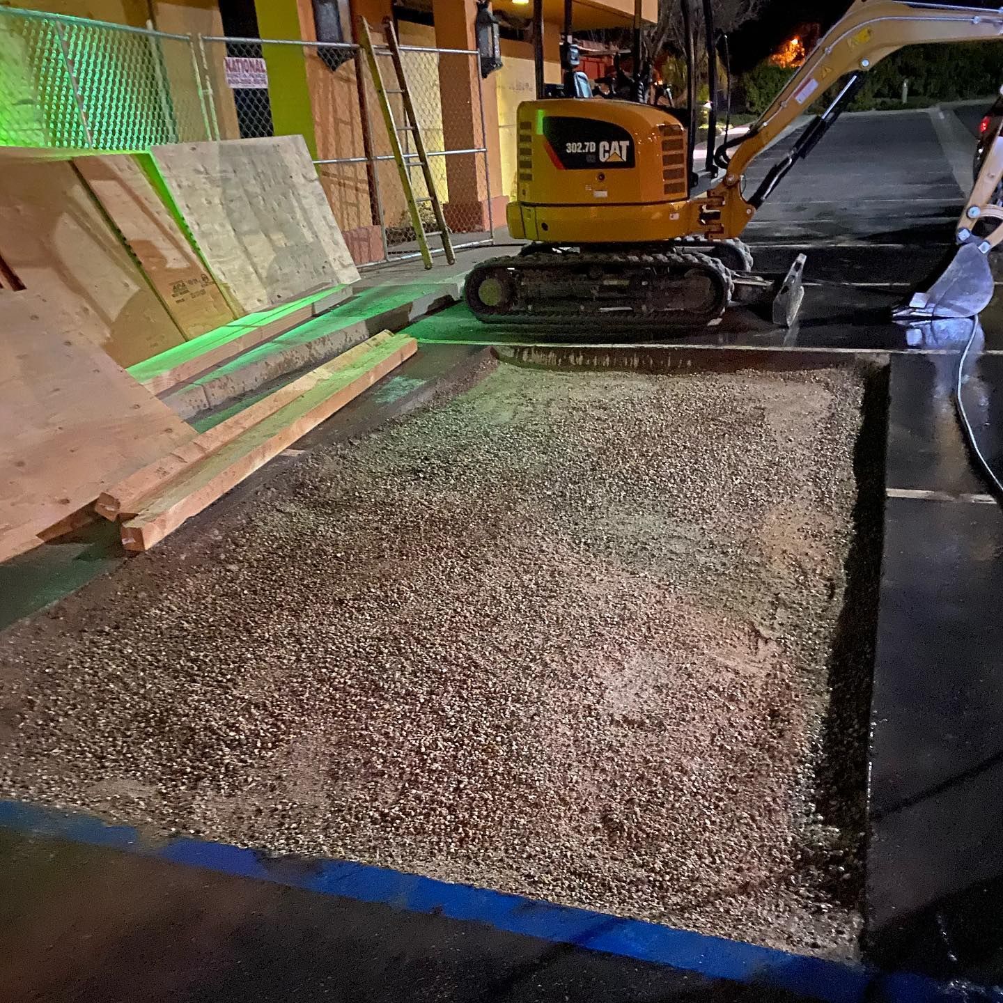 Small excavator on a parking lot. A rectangular section of asphalt is removed, filled with gravel.