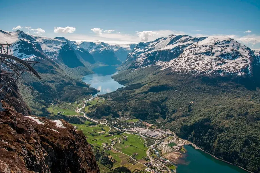 Utsikt over en dal omgitt av fjell og en innsjø fra toppen av et fjell.