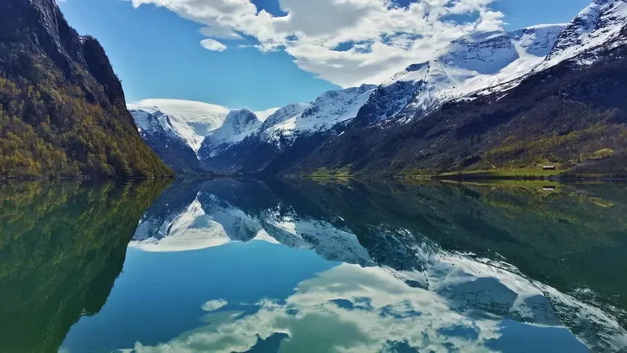 En innsjø omgitt av snødekte fjell reflekteres i vannet.