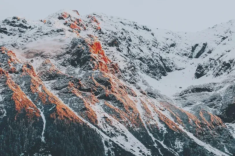 Et snødekt fjell med trær på siden av det