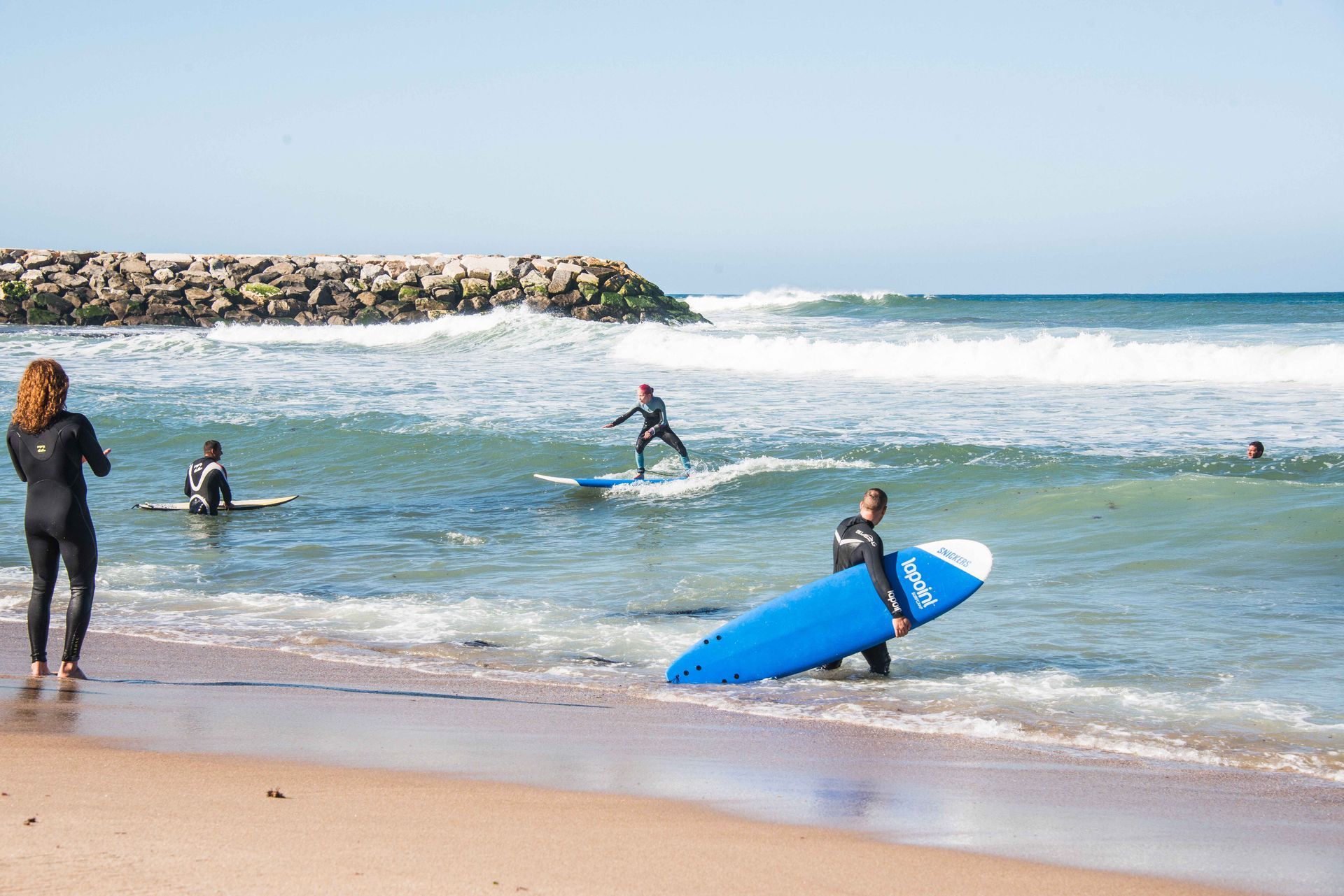 En gruppe surfere rir på bølger på stranden.