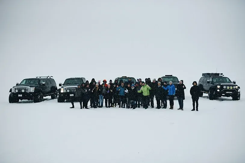 En gruppe mennesker poserer foran en bilrekke i snøen.