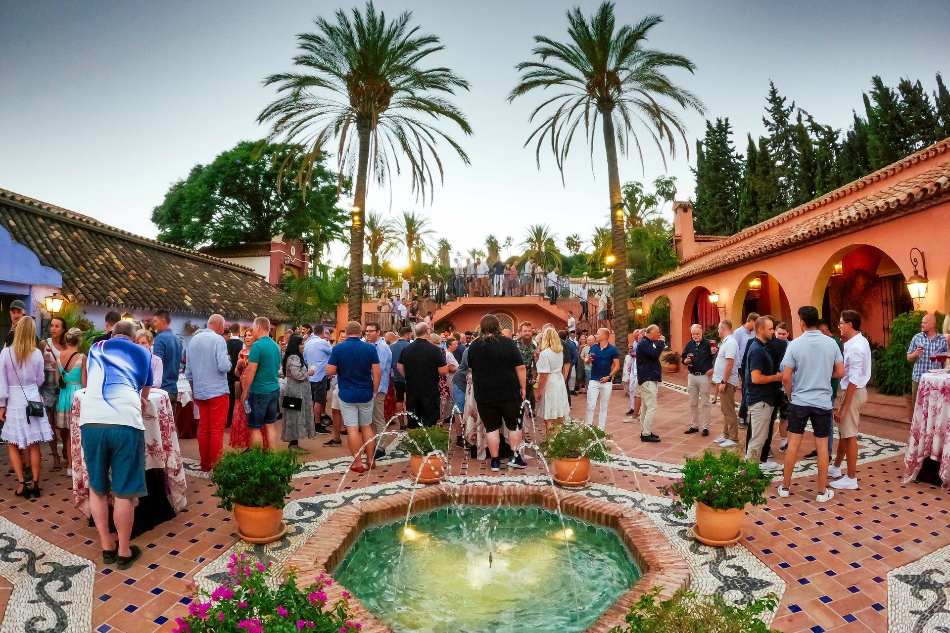 En gruppe mennesker står rundt en fontene på en gårdsplass.